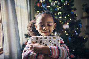 Christmas, holiday and young girl with gift, happy and thank you for present, celebration at family home. Child hug gift box, celebrate in house living room and festive mood, smile and happiness.