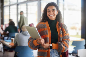 Smiling young female student standing with a laptop in a college cafeteria