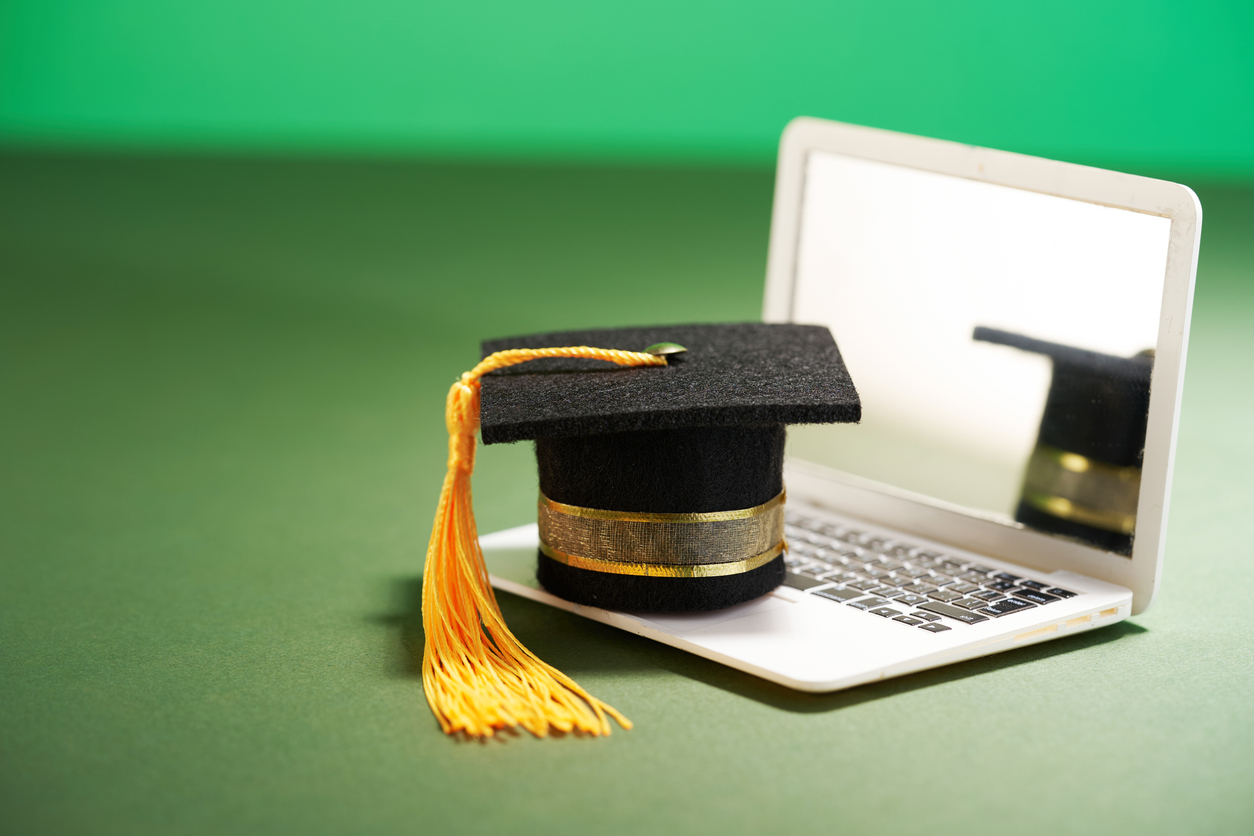 small mortarboard on the miniature laptop againnst green background