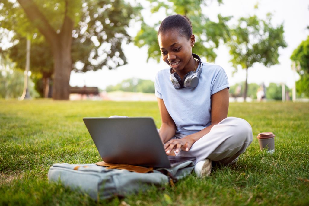 Young female University student of Black ethnicity e learning on laptop, at the campus park