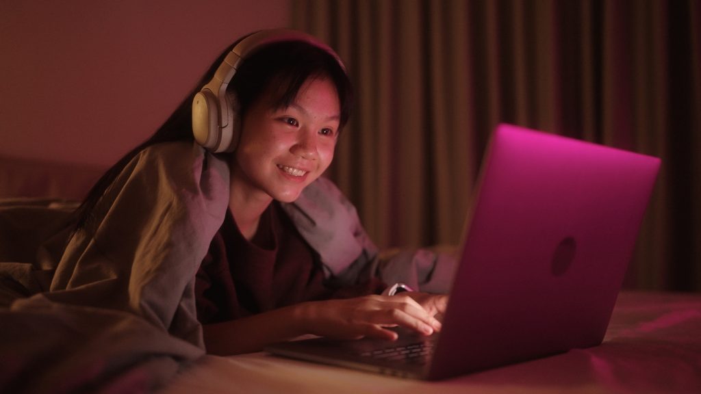 Teenage girl using laptop in bed at night.